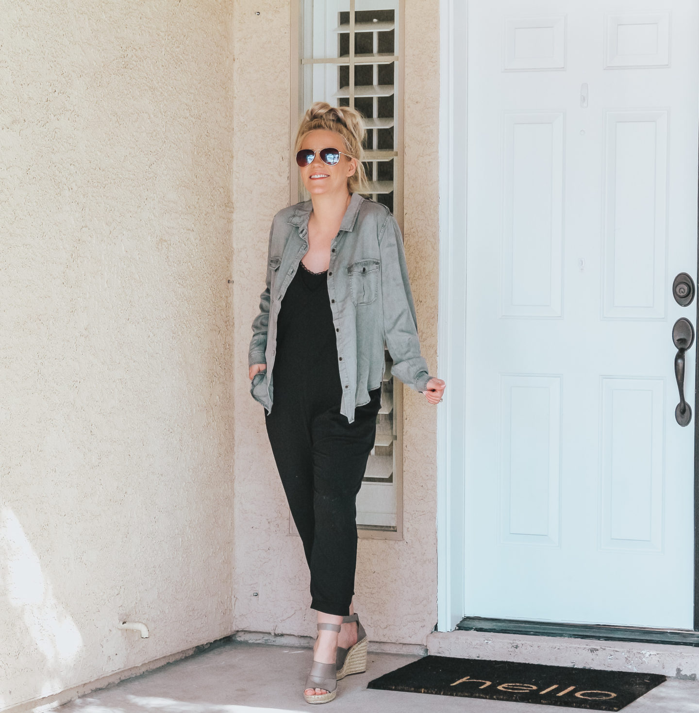 fashion blogger stonding by front door in a black jumpsuit and button up