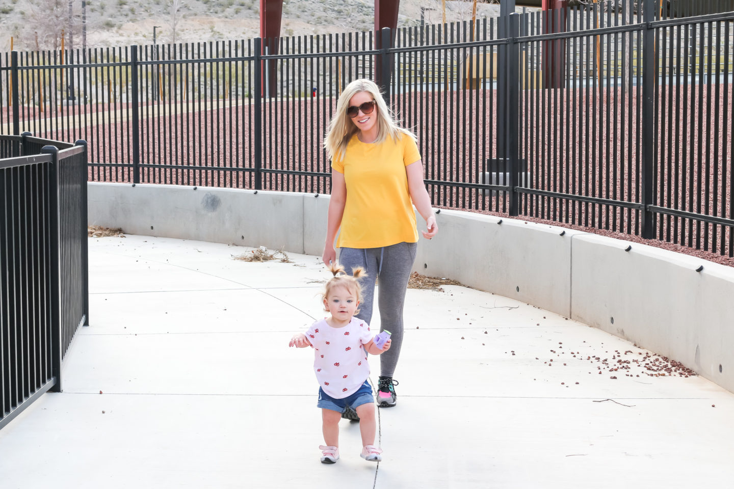 mom blogger walking down side walk with toddler daughter wearing spring outfits in yellow