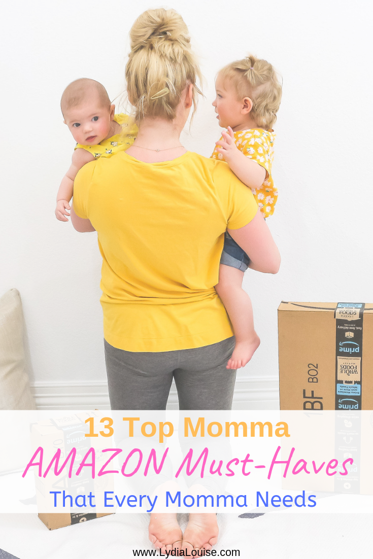 mom blogger on knees facing a white wall holding two babies by amazon packages